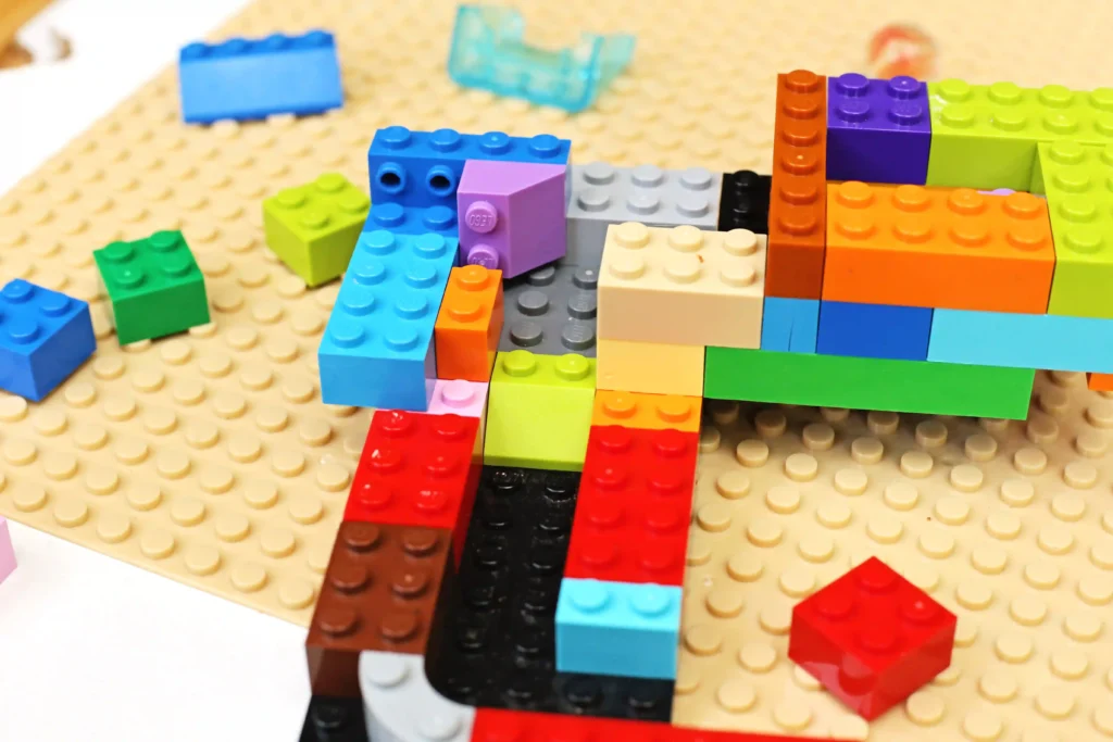 Colorful LEGO bricks stacked to form a small, multicolored structure on a tan studded baseplate, with scattered bricks nearby.