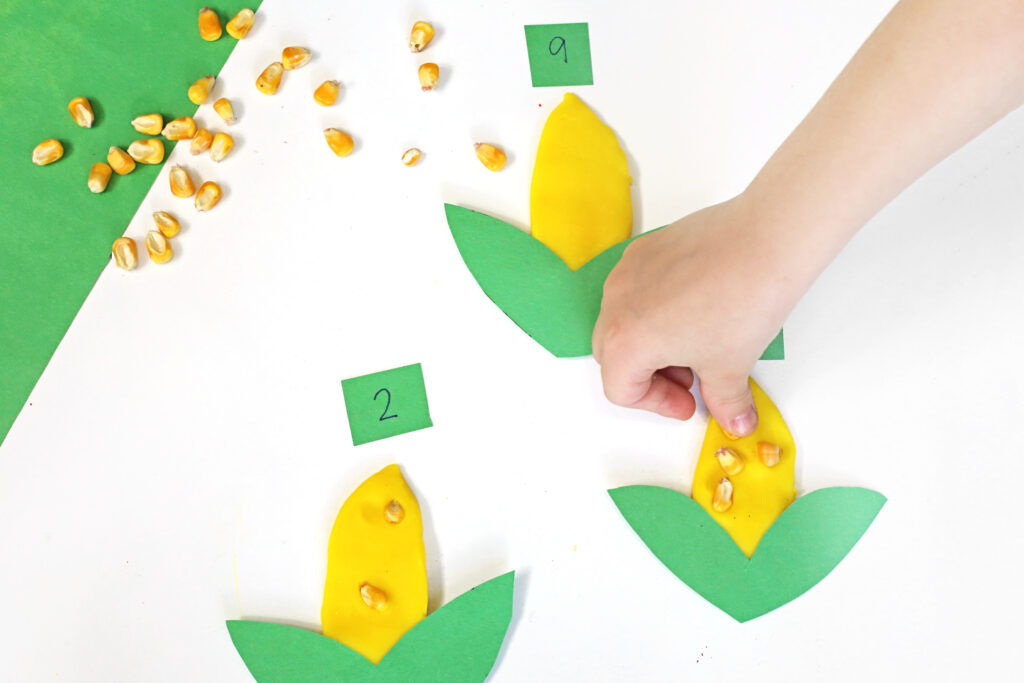 a kid pressing corn kernels into yellow playdough that looks like corn