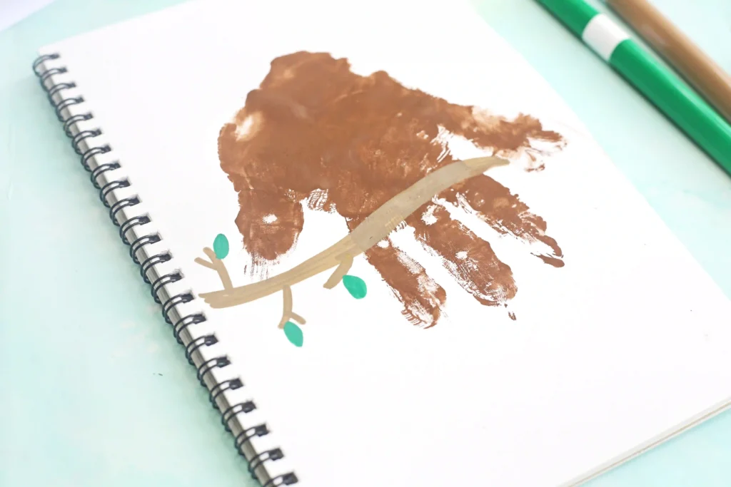 Spiral-bound notebook page with brown paint handprint with a branch drawn on