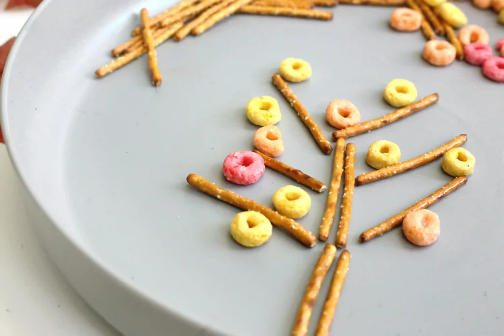 Colorful ring-shaped cereal pieces and pretzel sticks arranged on a light plate, like a snack arrangement.