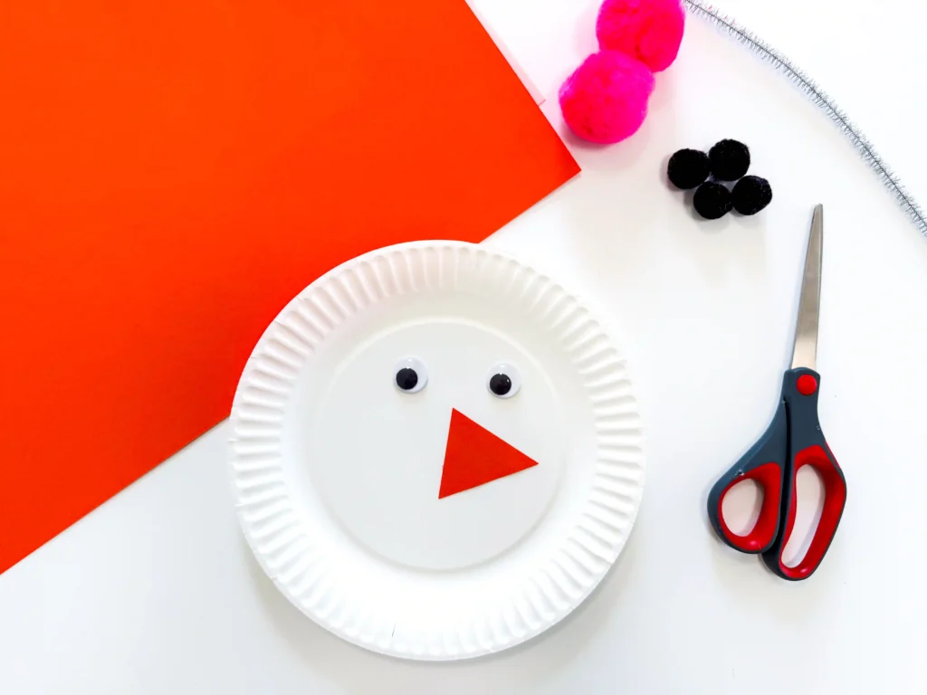 Paper Plate Snowman Craft - Cultivating Brilliant Minds paper plate with googly eyes and a triangle orange nose