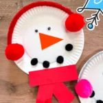 paper plate snowman craft of a paper plate decorated to look like a snowman with earmuffs and a scarf