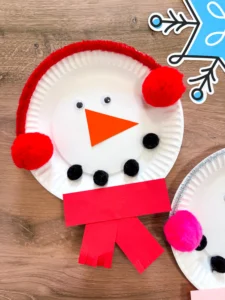 paper plate snowman craft of a paper plate decorated to look like a snowman with earmuffs and a scarf