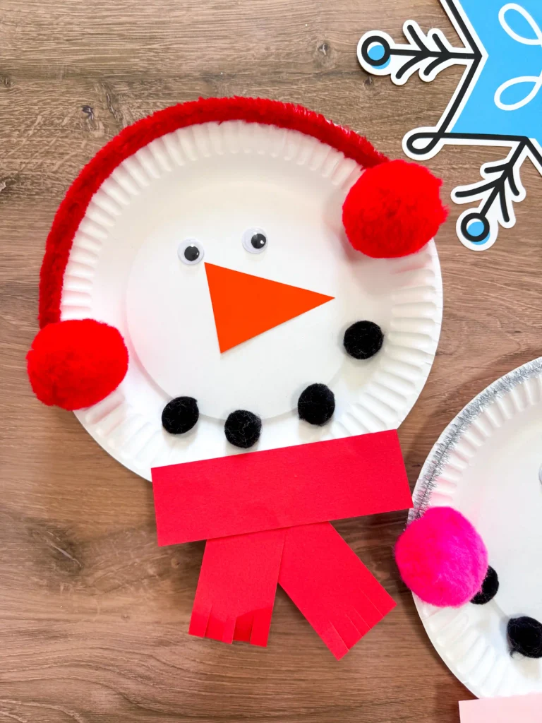 paper plate snowman craft of a paper plate decorated to look like a snowman with earmuffs and a scarf