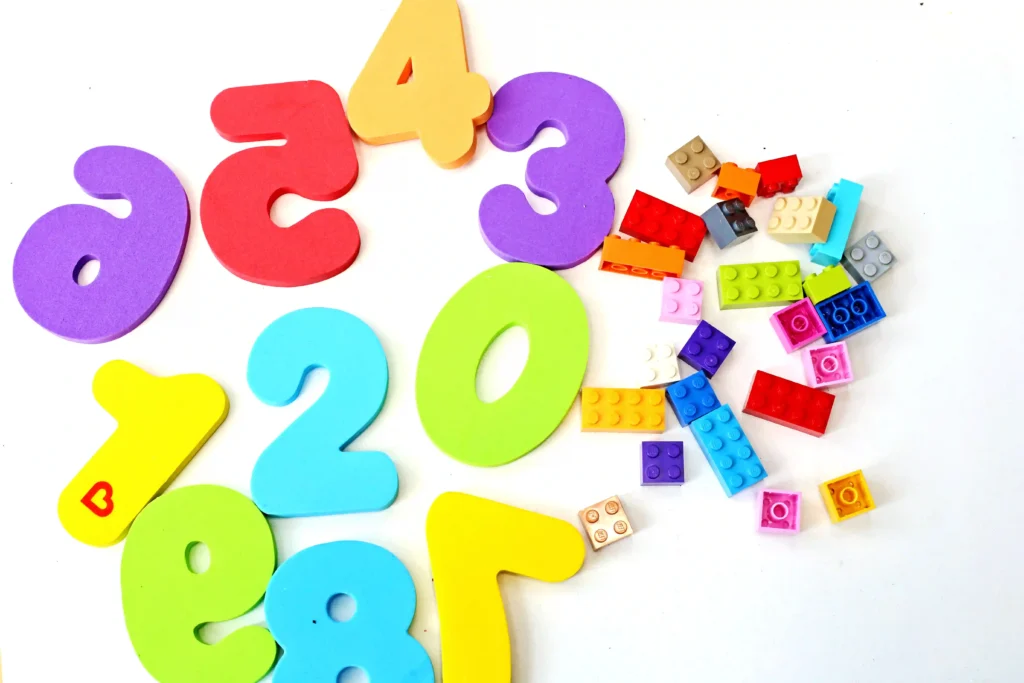 supplies for the lego math towers: Colorful foam numbers 0 through 9 scattered with small LEGO bricks on a white background.