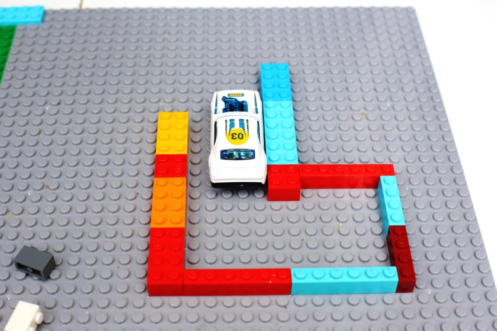 White LEGO race car on a colorful brick track on a gray baseplate, viewed from above.