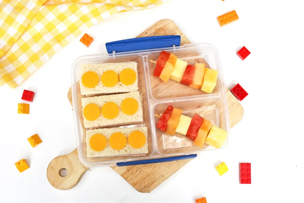 LEGO Lunchbox Idea - Cultivating Brilliant Minds a LEGO-themed Lunch box Idea that has sandwiches that look like legos and stacks of fruit