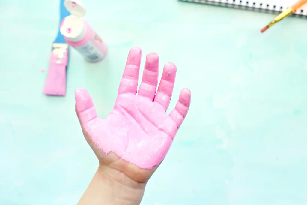 Raised left hand covered in pink paint against a pale turquoise background.