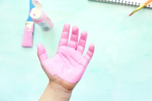 Raised left hand covered in pink paint against a pale turquoise background.
