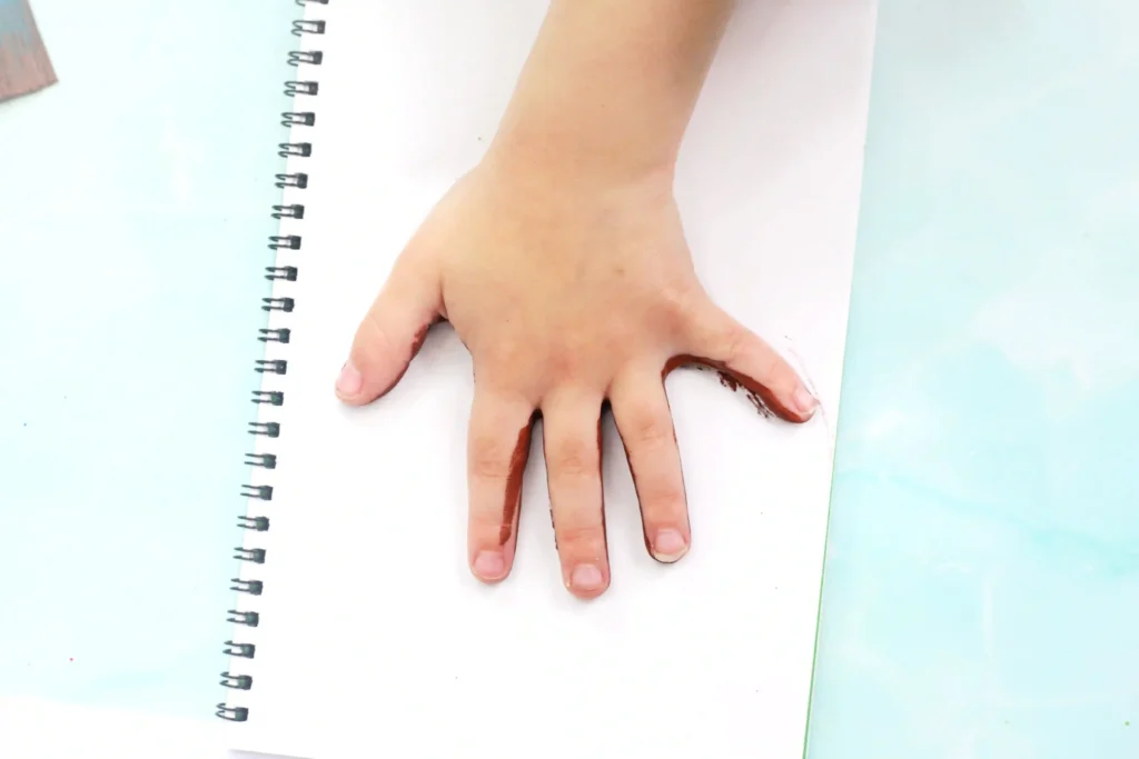 Top-down view of a small hand resting on an open spiral notebook with light blue background;