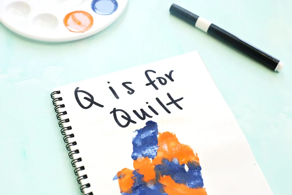 Spiral-bound notebook on a pale blue surface with blue and orange paint strokes and a nearby black marker.