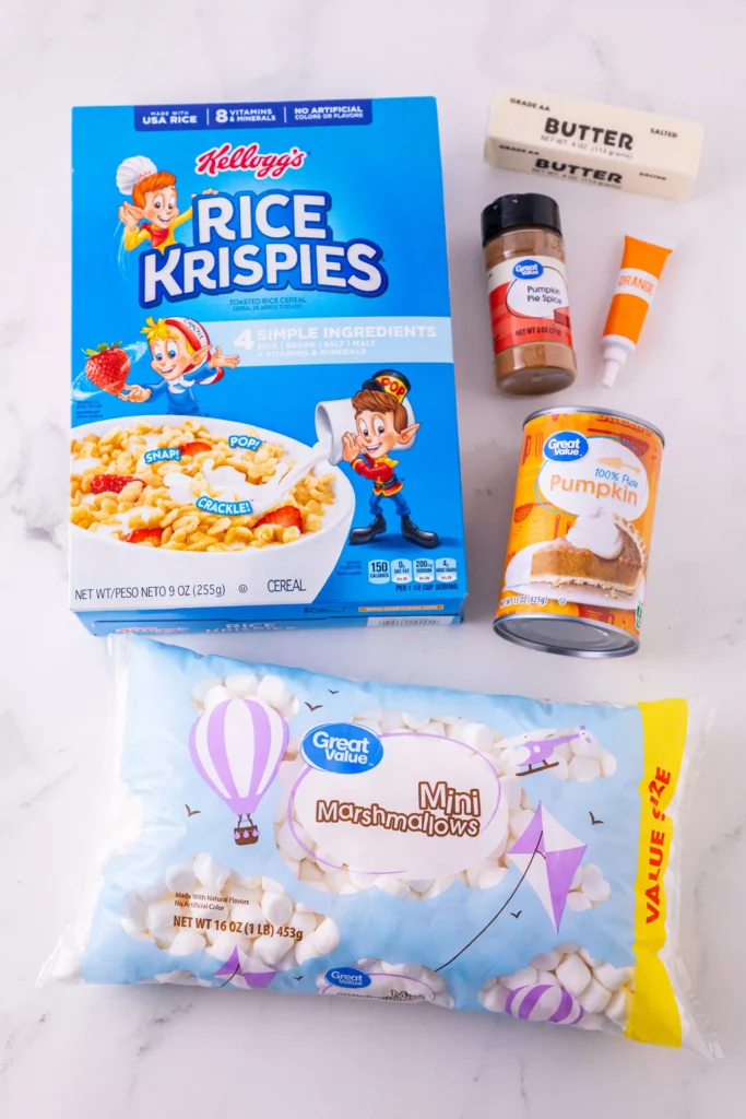 ingredients for the mini pumpkin pie rice krispie treats: Blue Kellogg's Rice Krispies cereal box with a strawberry and cartoon characters, next to butter, pumpkin pie spice, orange icing tube, pumpkin can, and a bag of mini marshmallows in a bright package.