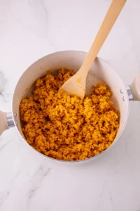 Pot of orange cooked rice krispies cereal with a wooden spoon resting inside the pan.