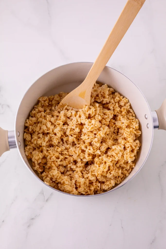 Pot of fluffy rice krispies cereal being stirred with a wooden spatula by a marble countertop
