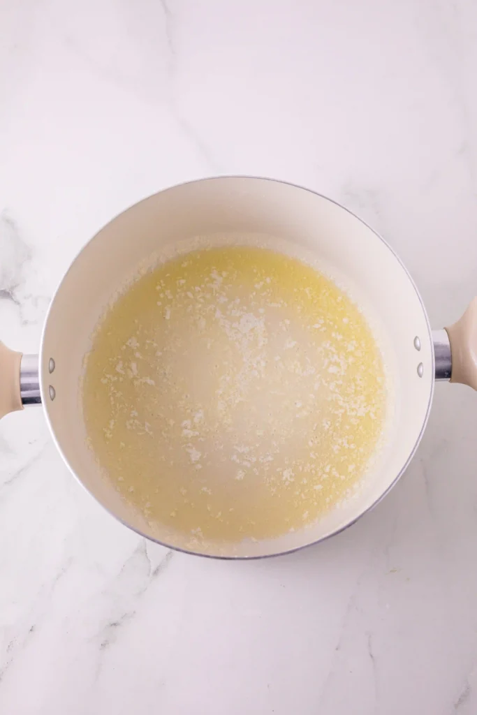 Top-down view of a white saucepan on a marble countertop, filled with pale melted butter