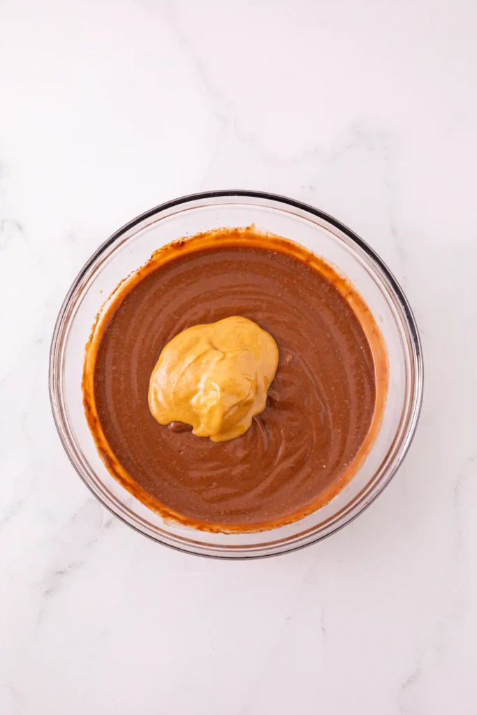 Top-down view of a glass bowl filled with pudding mix and a dollop of peanut butter on top, set on a white marble surface.