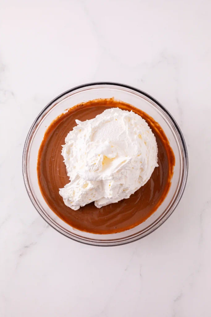 Top-down view of a glass bowl filled with chocolate pudding topped with whipped cream.