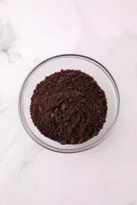 Top-down view of a glass bowl filled with dark brown coffee grounds on a white marble surface