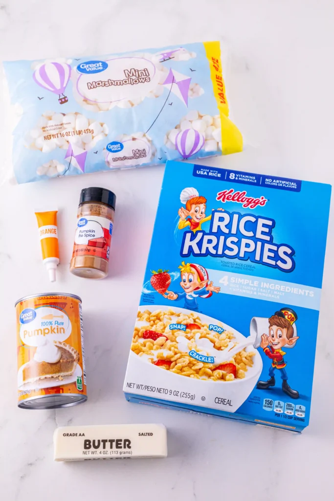 ingredients for the pumpkin pie rice krispies: Rice Krispies cereal, mini marshmallows, pumpkin spice, canned pumpkin, butter, and a squeeze tube on a white surface.