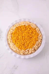 Top-down view of a white plate filled with yellow and orange rice krispie clusters in the center and lighter cereal around the edge on a marble surface.