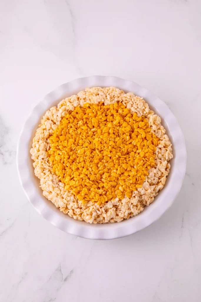 Top-down view of a white plate filled with yellow and orange rice krispie clusters in the center and lighter cereal around the edge on a marble surface.