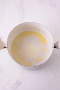Top-down view of a white pot with a thin ring of yellow butter sticking to the inside, on a white marble counter
