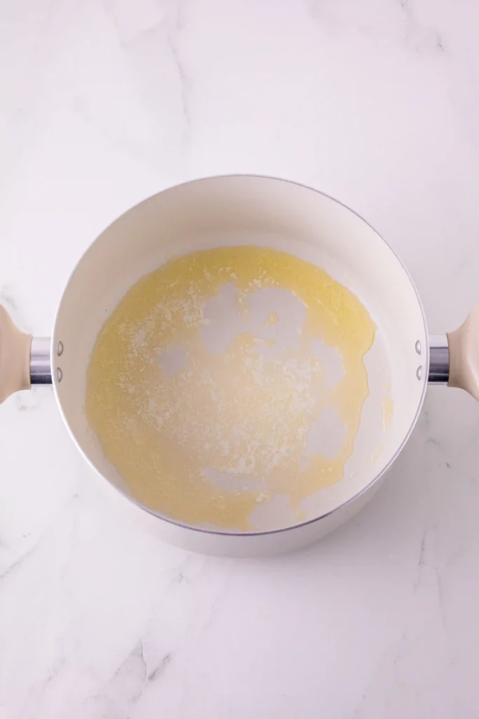 Top-down view of a white pot with a thin ring of yellow butter sticking to the inside, on a white marble counter
