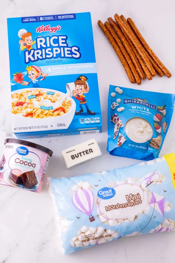 ingredients for the rice krispie turkey legs: Kellogg's Rice Krispies cereal box on a white surface with pretzel sticks and baking ingredients nearby (butter, cocoa, marshmallows).