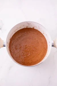 Overhead view of a white saucepan filled with brown batter, with batter splatters along the rim on a white marble surface.