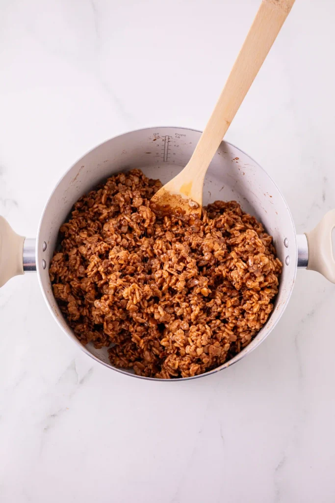 Top-down view of a pot filled with cooked brown rice krispies cereal and a wooden spoon resting inside.