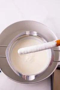 Stainless mixing bowl filled with white melted chocolate and a chocolate covered pretzel resting on the rim