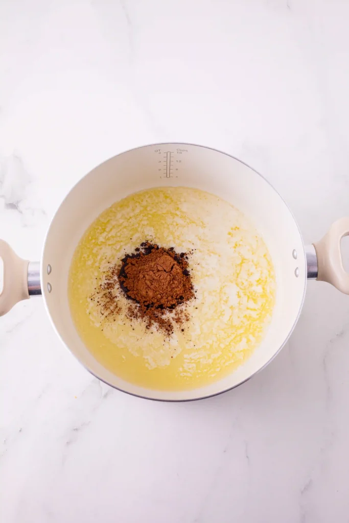 Top-down view of a white pot with pale yellow butter and a scoop of brown cocoa powder on top, resting on a marble surface.