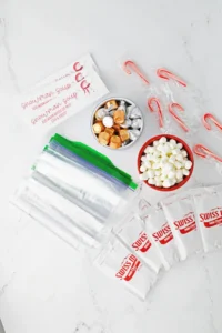 ingredients for the snowman soup: candy canes, foil-wrapped chocolates, marshmallows, and Swiss chocolate packaging on a white surface