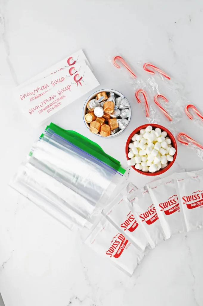 ingredients for the snowman soup: candy canes, foil-wrapped chocolates, marshmallows, and Swiss chocolate packaging on a white surface