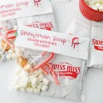 Swiss Miss hot cocoa packets labeled 'Snowman Soup' with marshmallows and candy canes on a white surface.