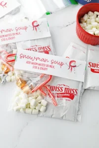 Swiss Miss hot cocoa packets labeled 'Snowman Soup' with marshmallows and candy canes on a white surface.