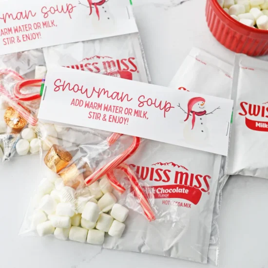 Swiss Miss hot cocoa packets labeled 'Snowman Soup' with marshmallows and candy canes on a white surface.