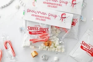 Assorted holiday treats around Swiss Miss hot chocolate packets on a white surface, including candy canes and foil-wrapped candies.