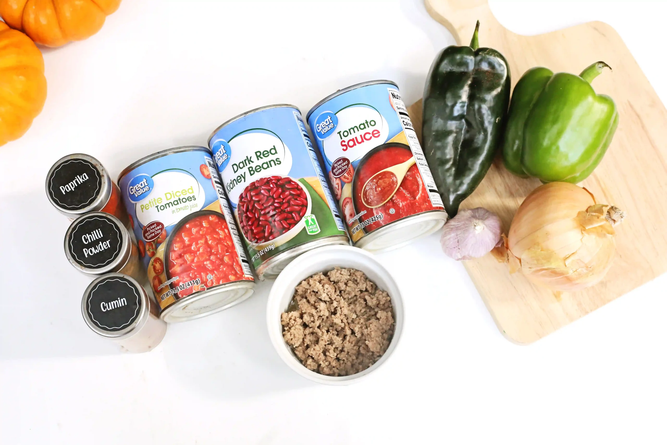Canned tomato sauce and kidney beans with peppers, onions, garlic, and spices on a cutting board; meat in a bowl nearby (prep ingredients)