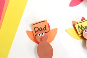 Orange paper turkey with googly eyes and a 'Dad' label, part of a colorful paper craft.