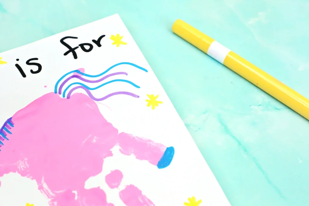 Colorful desk scene with a spiral notebook, a handprint unicorn on the page