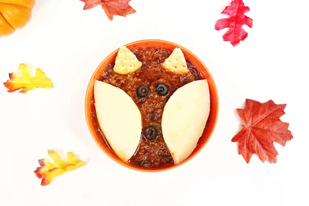a bowl of chili with crackers and olives on top to look like a fox