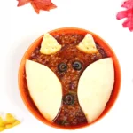 a bowl of chili with crackers and olives on top to look like a fox