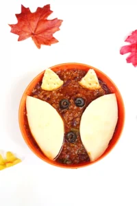 a bowl of chili with crackers and olives on top to look like a fox