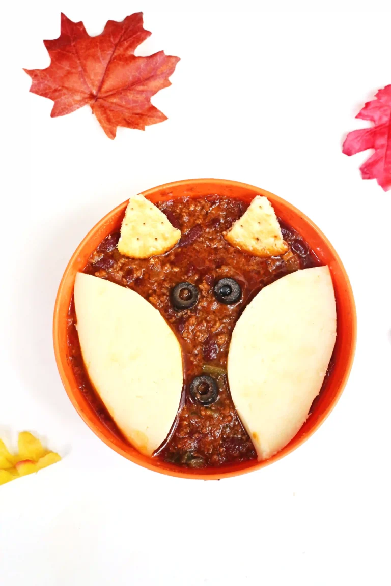a bowl of chili with crackers and olives on top to look like a fox