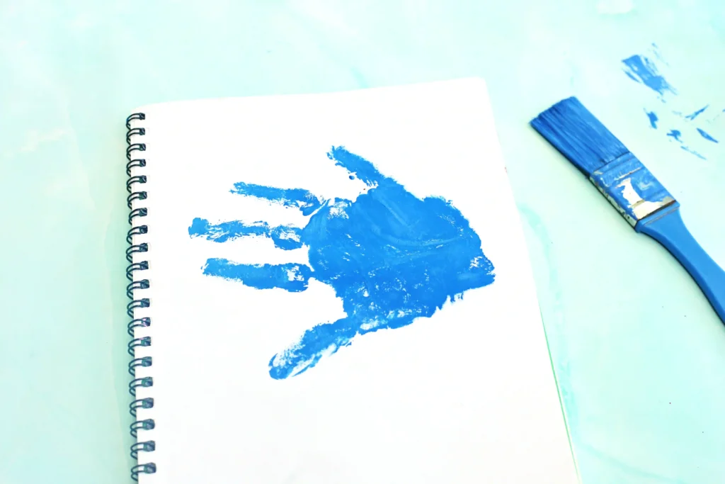 White spiral notebook page smeared with blue paint, with a blue paintbrush resting to the right.