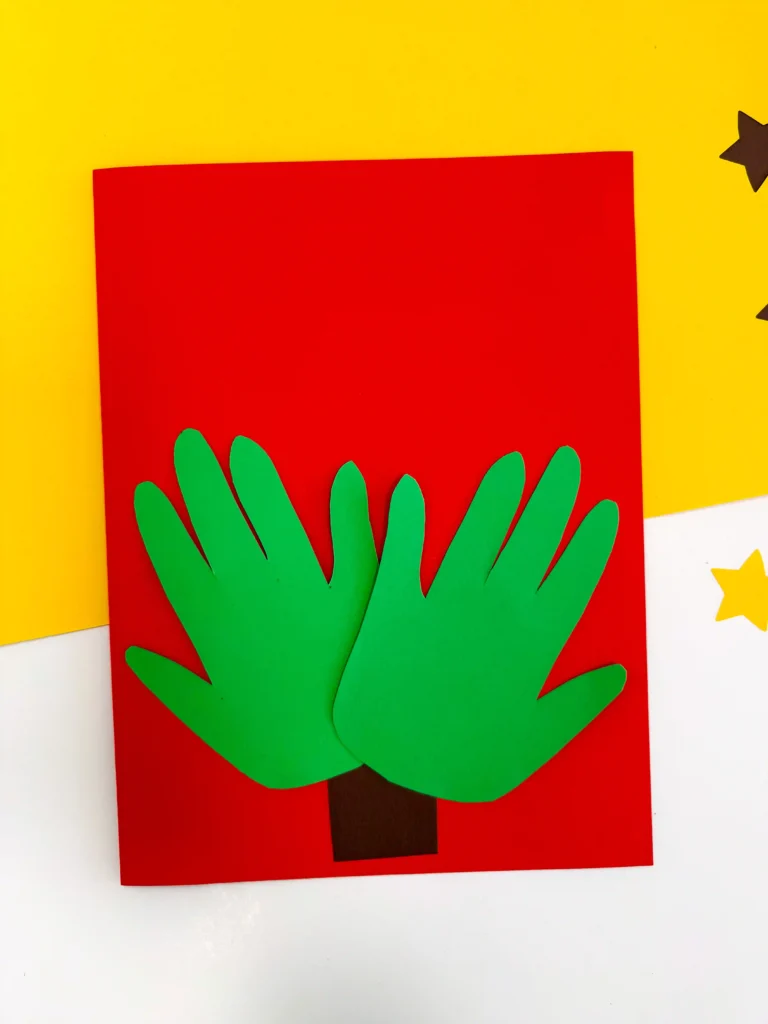 red construction paper with a brown tree trunk and green handprints