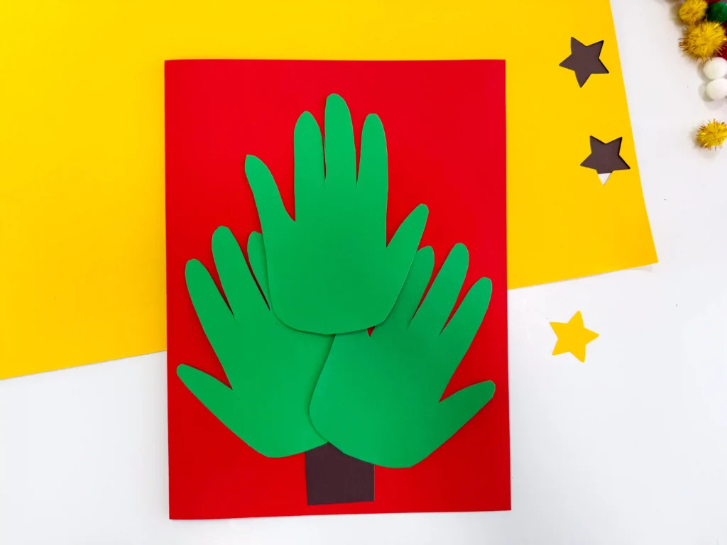 red construction paper with a brown tree trunk and green handprints