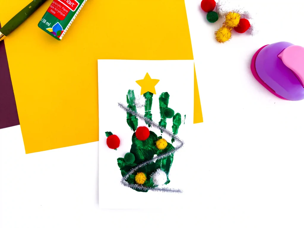 a Handprint Christmas Tree Card made with a green handprint, pipe cleaner, and pom poms