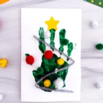 a Handprint Christmas Tree Card made with a green handprint, pipe cleaner, and pom poms